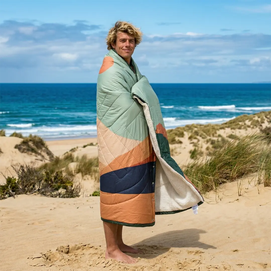 Surfer wrapped in a VOITED CloudTouch blanket on a beach in southwest France