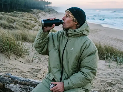 VOITED Drycoat 3.0 Changing Robe Surfer drinking from a flask wearing a VOITED Drycoat 3.0 Changing Robe