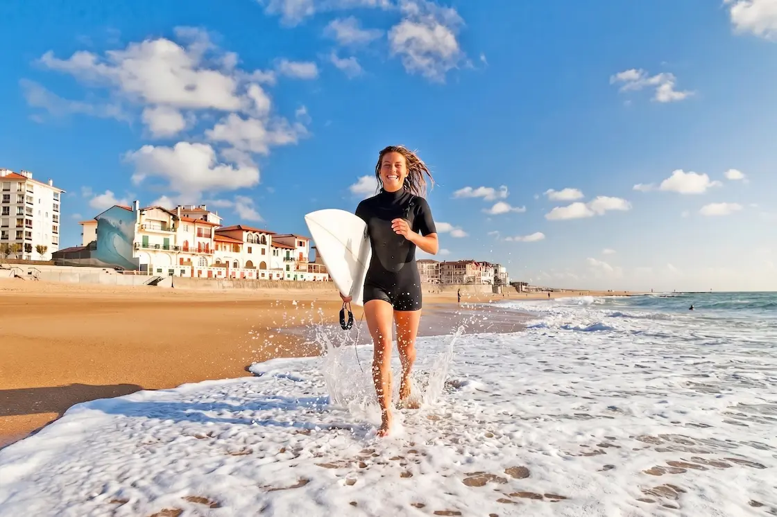 Camille running down the beach with her surfboard at Plage Centrale in Hossegor, France